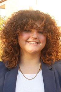 woman with curly red hair and lip piercing wearing a dark grey suit jacket